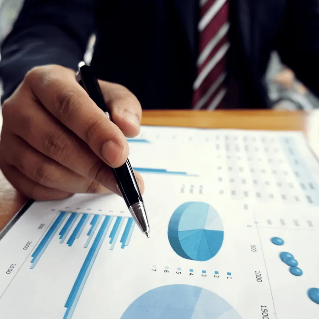 Imagem de mão segurando caneta sobre papel com gráficos ilustrando o fechamento contábil.