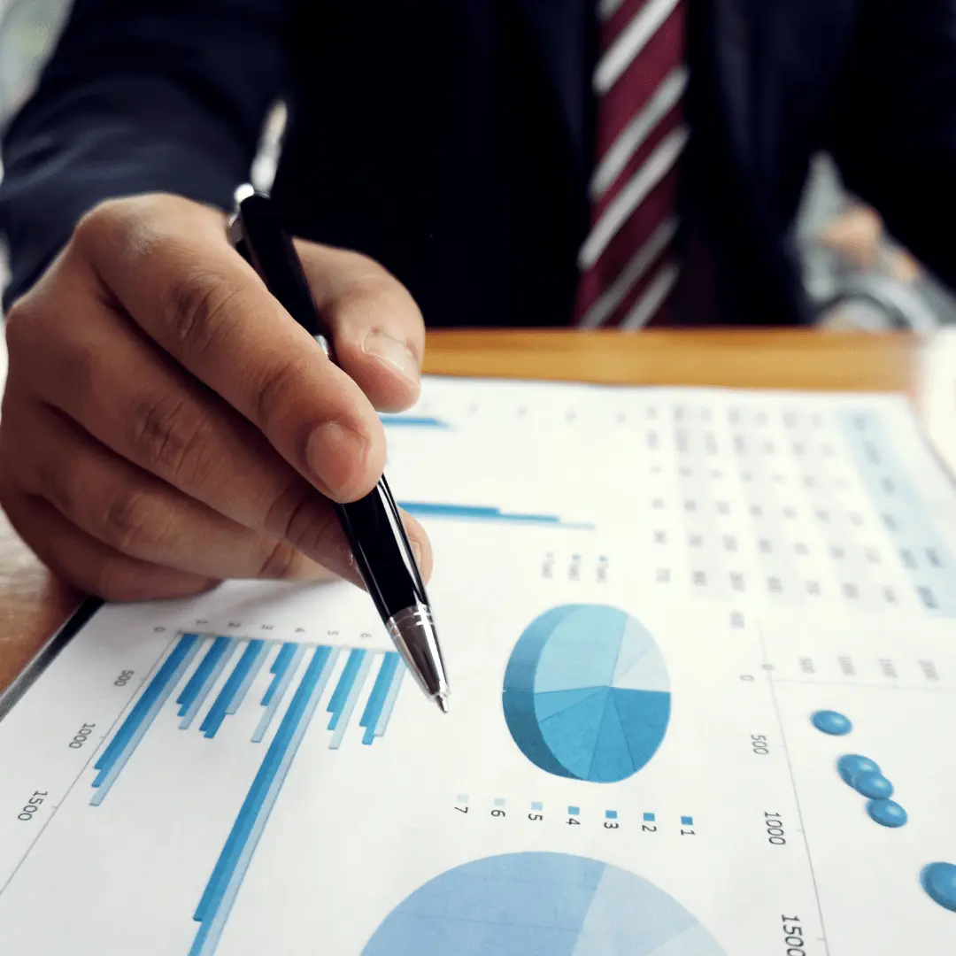 Imagem de mão segurando caneta sobre papel com gráficos ilustrando o fechamento contábil.