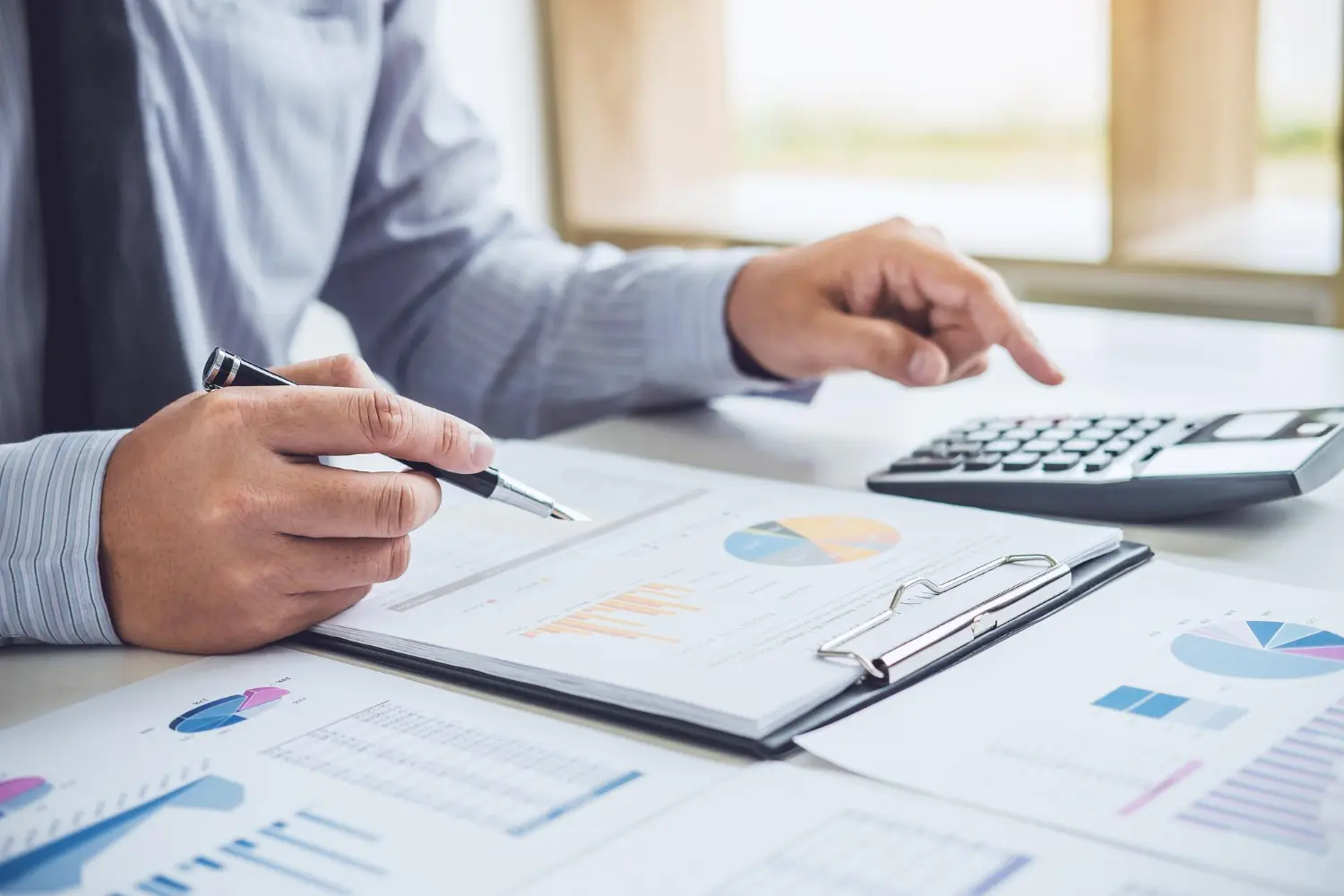 Contador analisando relatórios contábeis com gráficos e calculadora sobre a mesa de trabalho