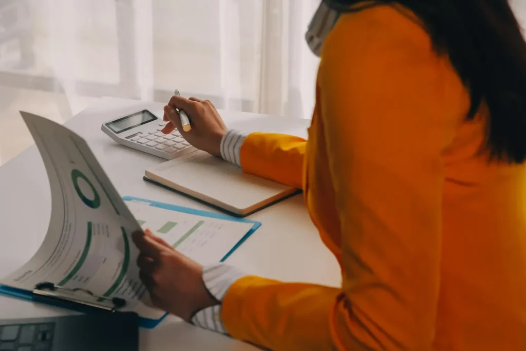 Contabilidade de custos com profissional analisando relatórios com calculadora e caderno no escritório