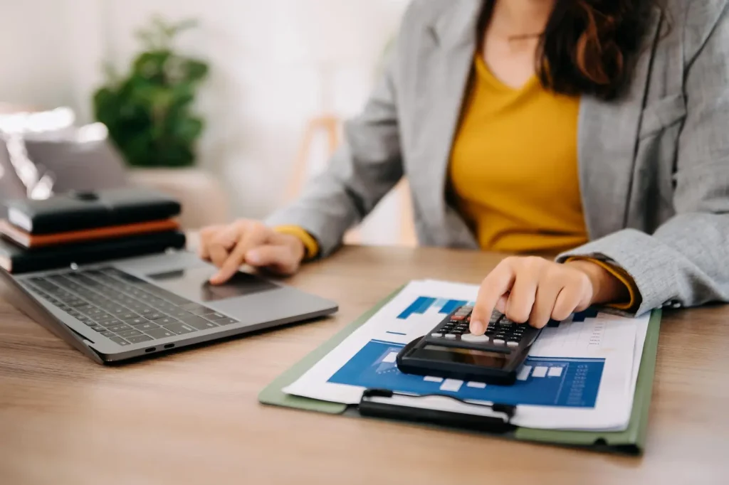 Profissional analisando crédito fiscal com calculadora, notebook e planilhas financeiras sobre a mesa.