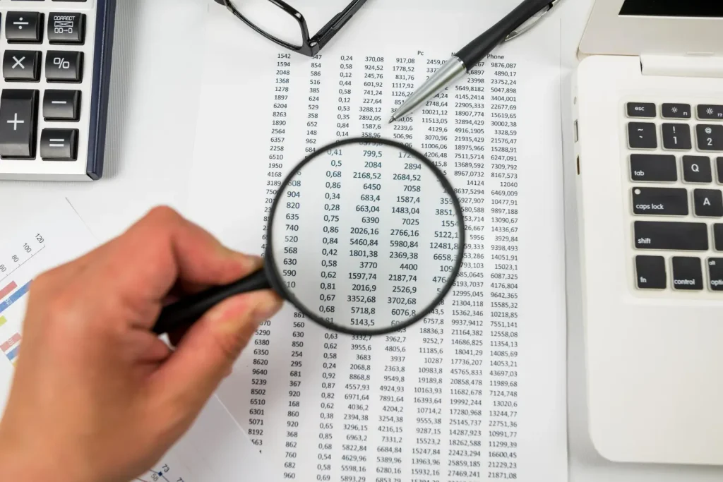 Imagem de um contador analisando números do balancete contábil com uma lupa.