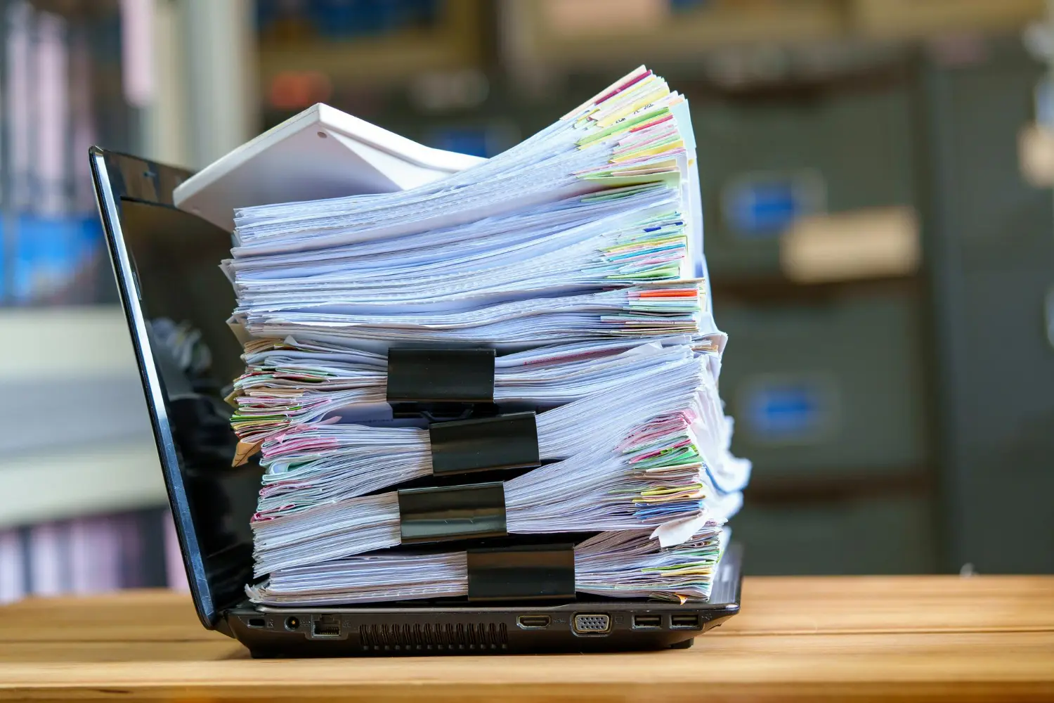 Imagem de uma pilha de documentos sobre um notebook, simbolizando a gestão documental na contabilidade.