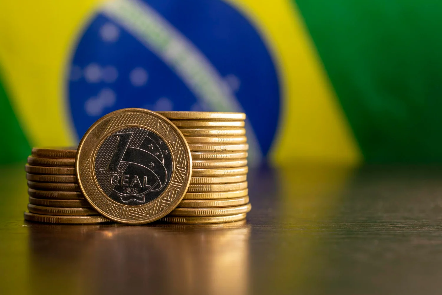 Imagem de uma pilha de moedas sobre a mesa com uma bandeira no Brasil no fundo, simbolizando o Simples Nacional.
