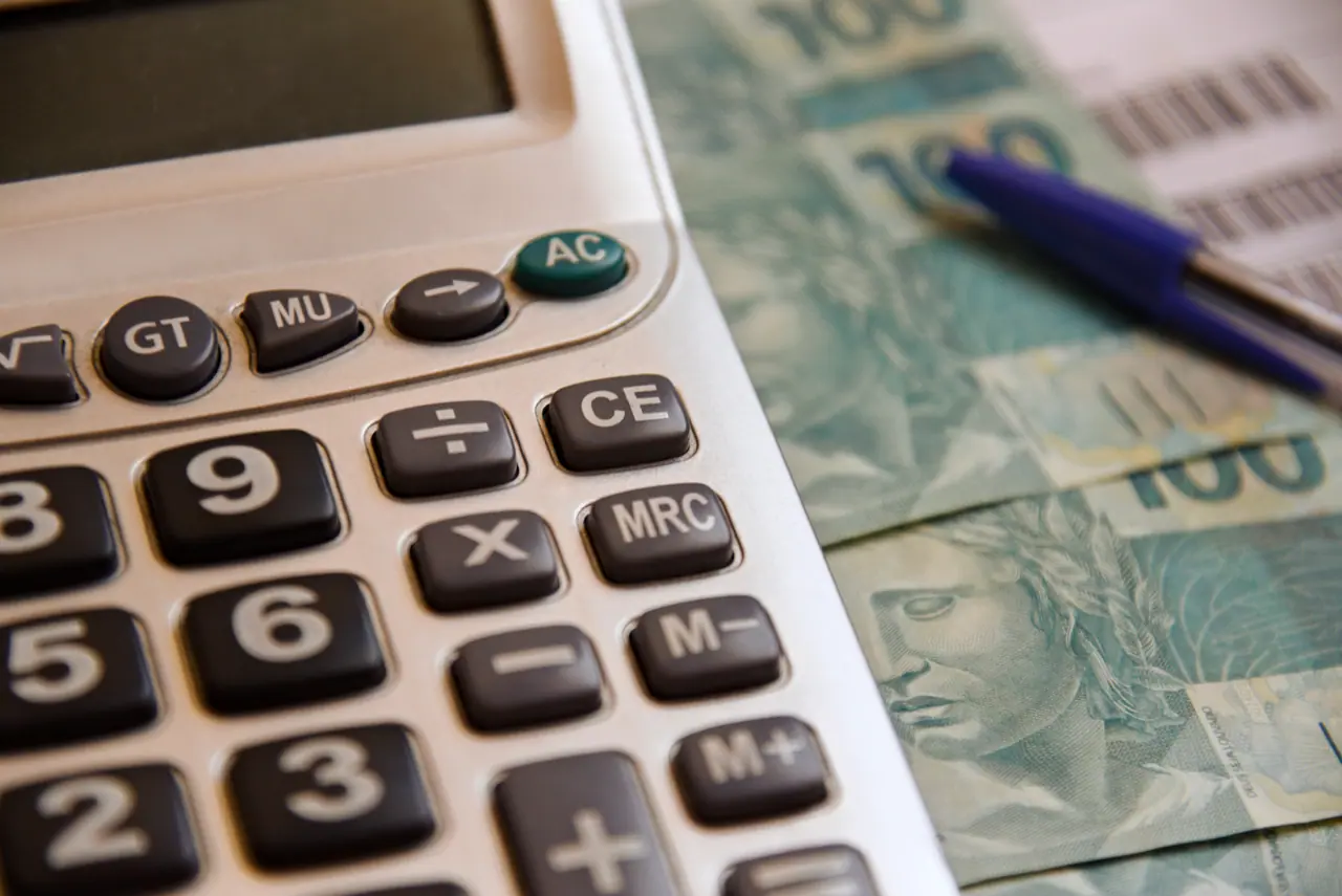 Imagem de uma calculadora, cédulas de dinheiro e uma caneta, simbolizando a análise de custo para abrir uma empresa.