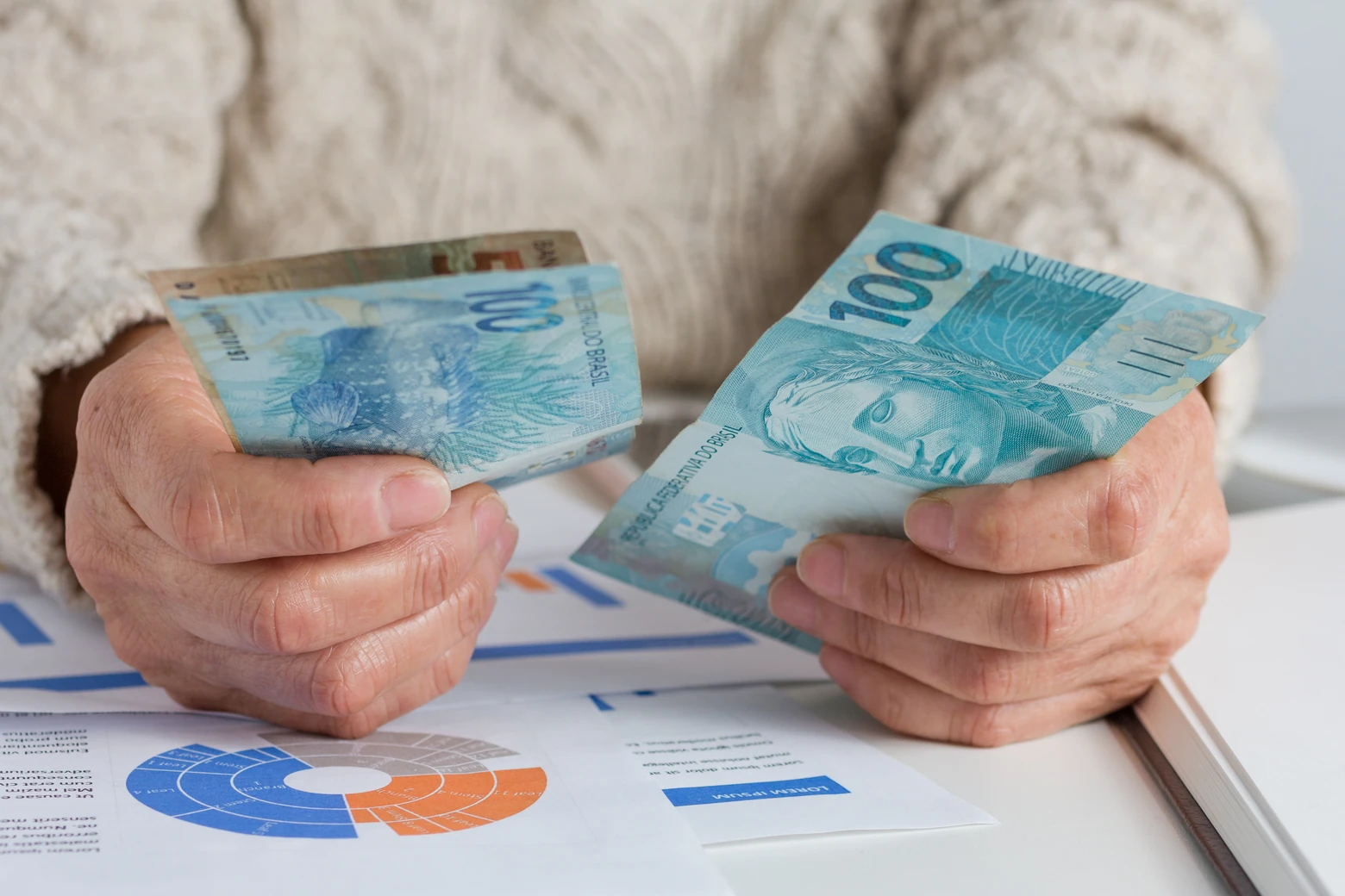 Homem conta notas de cem reais sob relatórios de distribuição de lucros