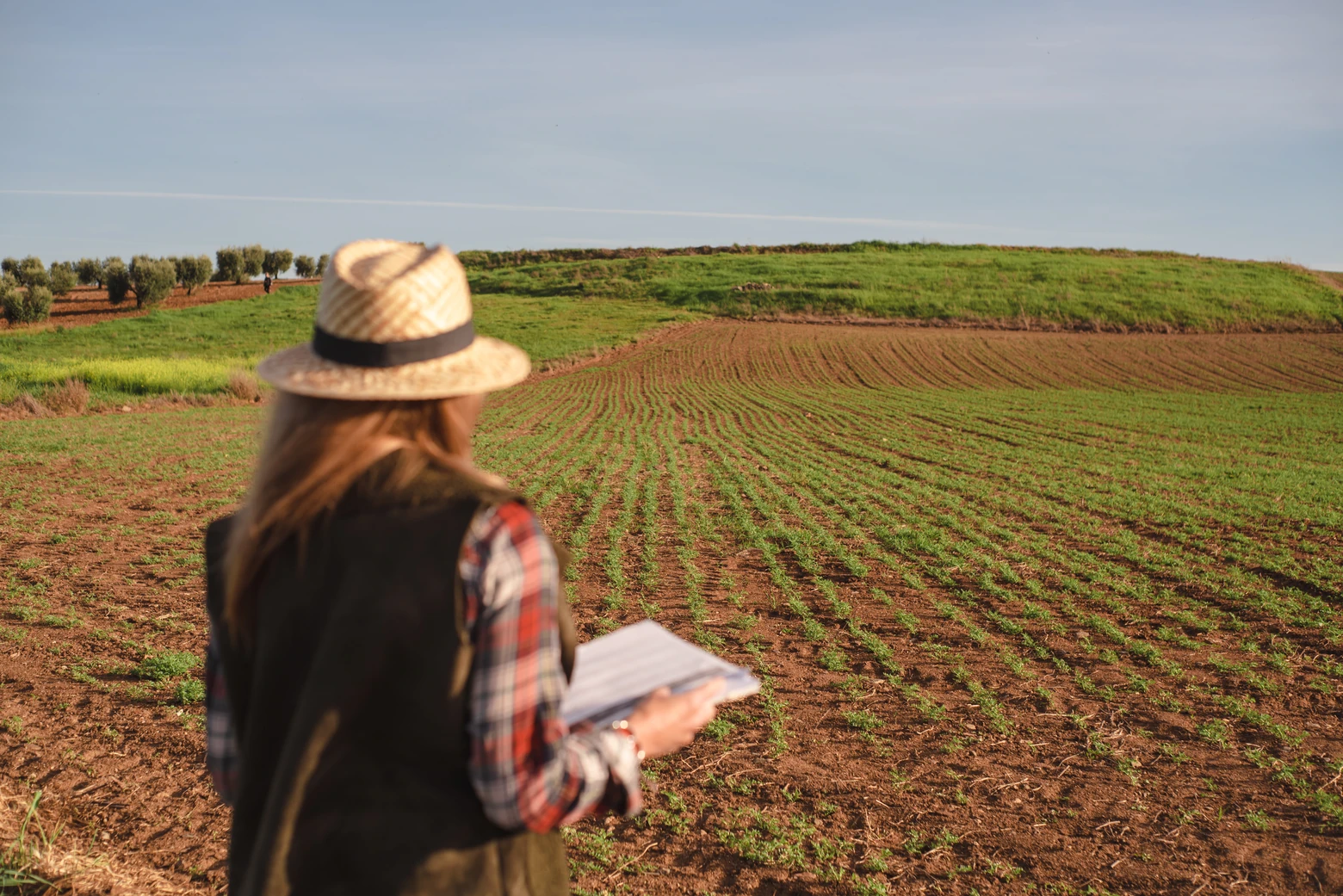 Produtora rural com documentos de DITR em mãos enquanto olha para o campo