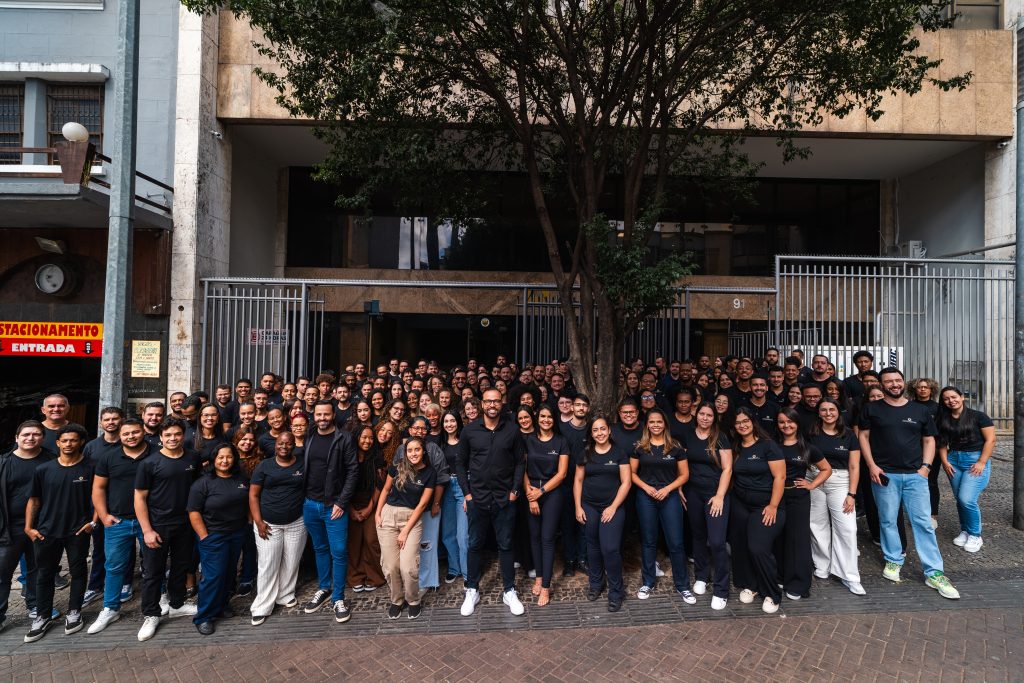 Equipe da Acessórias reunida em foto de grupo em frente à sede da empresa, com colaboradores vestindo camisetas pretas com o logo da marca.