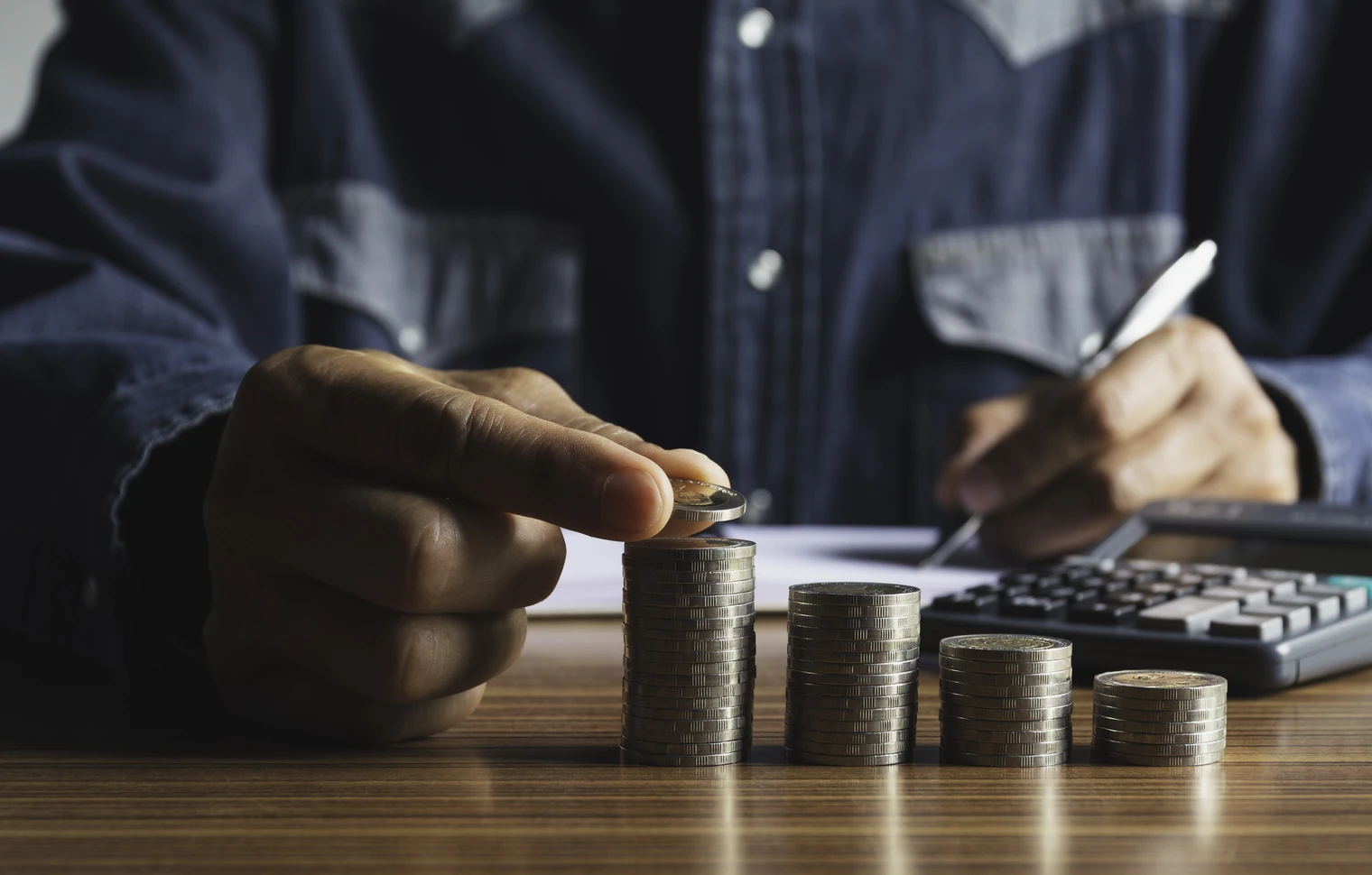 Profissional organiza moedas em pilhas enquanto usa uma calculadora para calcular tributação de dividendos